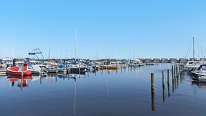 A marina with various boats docked, calm water, and a clear sky.