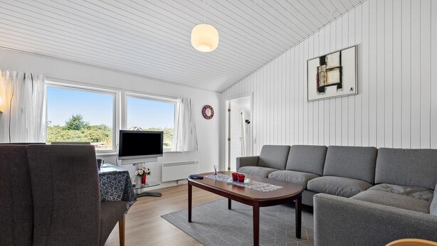 A modern living room with a grey sofa, a wooden coffee table, and a TV on a stand.