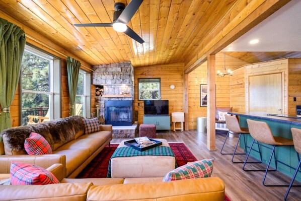 Un intérieur de chalet chaleureux avec une cheminée en pierre, des canapés en cuir, un coin repas et un bar.