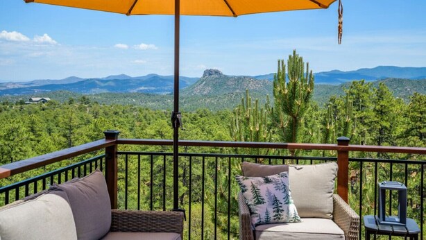 A balcony with a yellow umbrella, wicker furniture, and a view of a mountainous landscape. - Breathtaking Views. Elevated Comfort. Pets Welcome (Prescott)