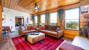 A cozy living room with a wooden ceiling, a large window with a view, and a fireplace. - Breathtaking Views. Elevated Comfort. Pets Welcome (Prescott)