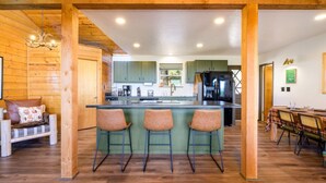 A cozy kitchen with a central island, green cabinets, and a dining area with a table and chairs. - Breathtaking Views. Elevated Comfort. Pets Welcome (Prescott)