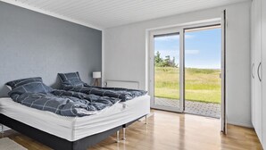 Et soveværelse med en seng, et natbord, en lampe og udsigt til en græsplæne gennem en skydedør.
