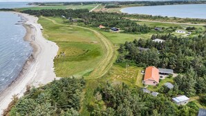Oversigtsbillede af en ejendom ved kysten med strand, grønne marker og flere huse.