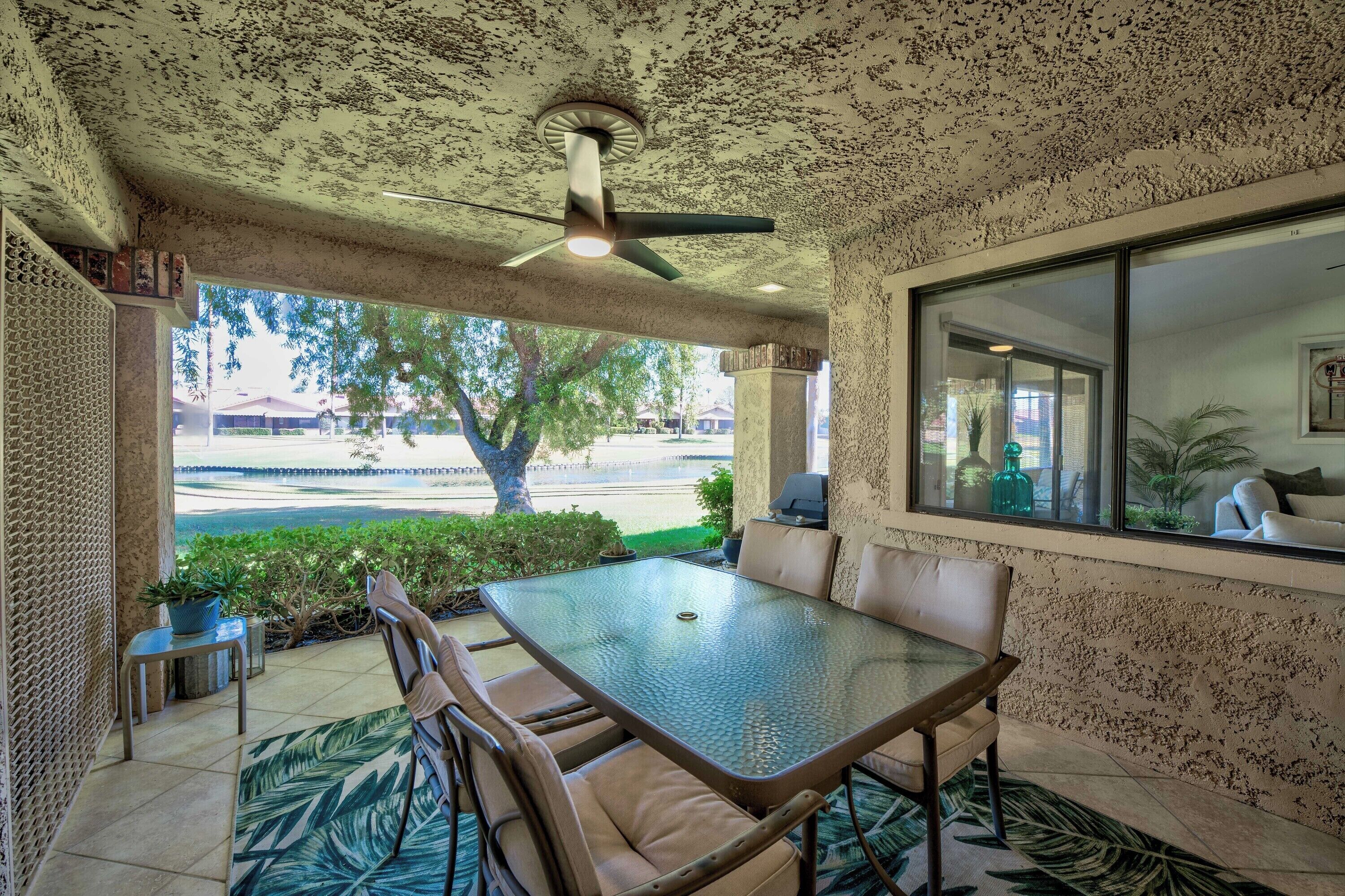 A covered patio with a glass table and chairs, a ceiling fan, and a view of the beach.