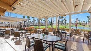 Eine Außenpatio-Terrasse mit Tischen und Stühlen, mit Blick auf einen Golfplatz und ein Gewässer.