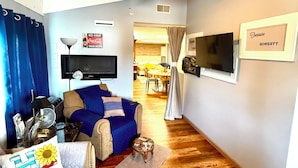 A living room with a blue sofa, a brown sofa, a ceiling fan, a TV, and a sign on the wall. - Modern 2 Bed Suite on Bourbon Trail (Loretto)