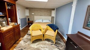 A bedroom with a bed, two wicker chairs, a dresser, a nightstand, and a cabinet. - Modern 2 Bed Suite on Bourbon Trail (Loretto)