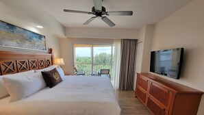 Ein Hotelzimmer mit einem großen Bett, einem Deckenventilator, einem Fernseher und einem Balkon mit Blick auf Bäume.