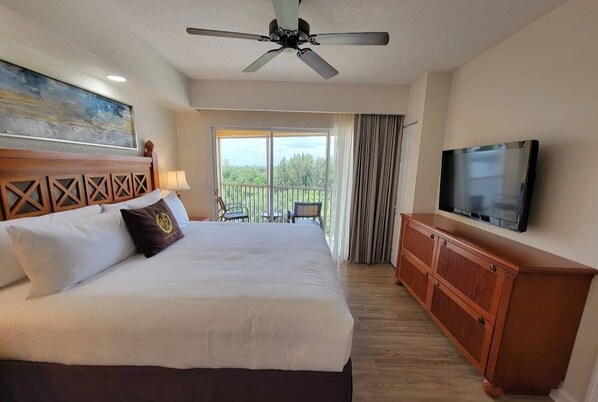 A hotel room with a large bed, a ceiling fan, a TV, and a balcony with a view of trees. - 2BR Villa, Beautiful heated pool & Jacuzzi!  Just minutes from all attractions.  (Kissimmee)