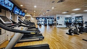 Ein Fitnessstudio mit Laufbändern an der Wand, einem Gewichtheberbereich und Trainingsgeräten.