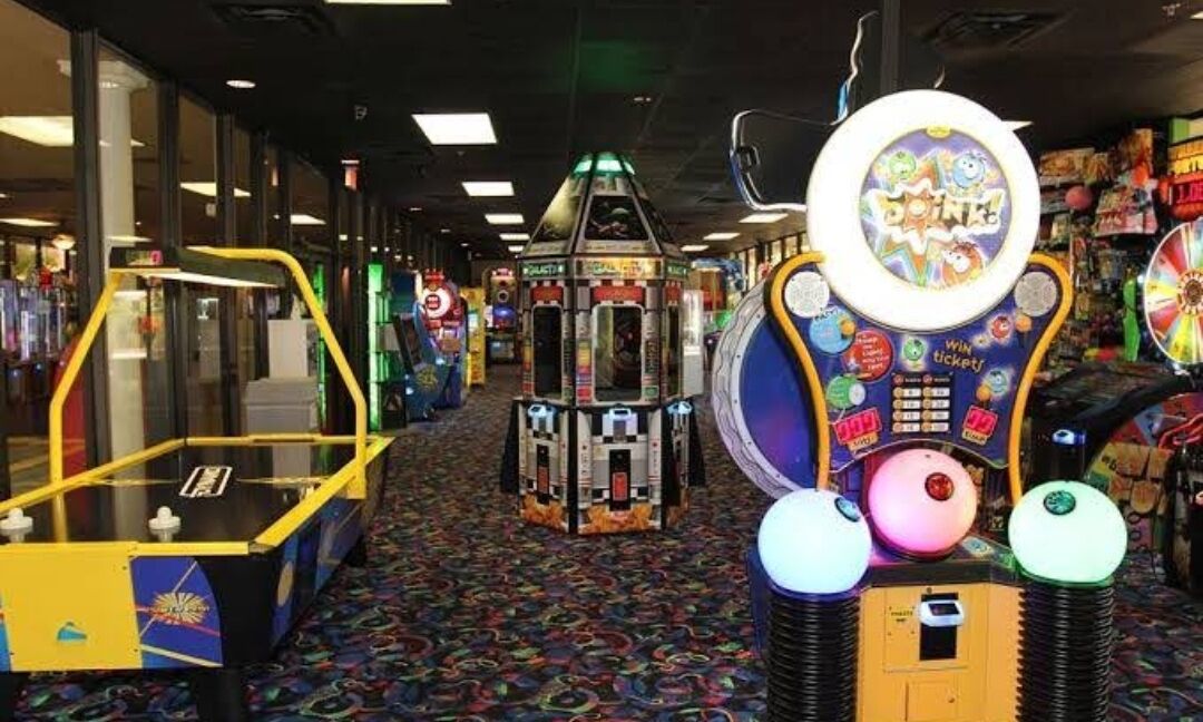 Une rangée de jeux d’arcade dans un espace intérieur bien éclairé, avec un tapis à motifs.