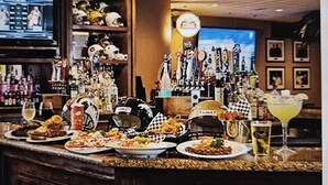 Eine Bar mit einer Auswahl an Speisen und Getränken auf der Theke, einem Fernsehbildschirm und einer Wand mit gerahmten Bildern.