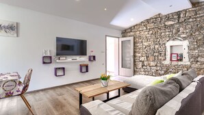 A modern living room with a stone wall, a flat-screen TV, a wooden coffee table, and a sofa. - Vacation home Nina by Interhome (Barban)