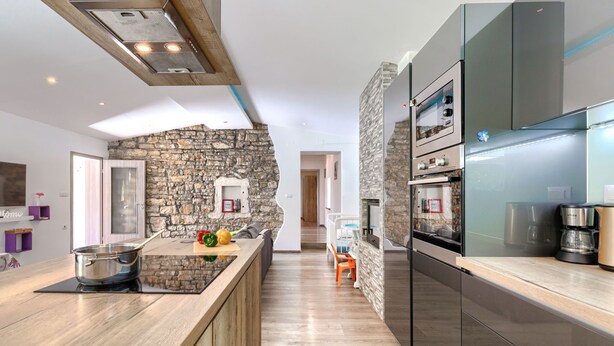 A modern kitchen with a stone accent wall, a wooden island, and a built-in oven. - Vacation home Nina by Interhome (Barban)