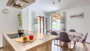 A modern kitchen with a wooden island, a dining area with a table and chairs, and a view of the outdoors. - Vacation home Nina by Interhome (Barban)
