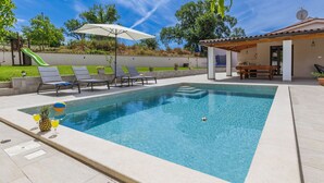 A swimming pool with lounge chairs and a covered patio area. - Vacation home Nina by Interhome (Barban)