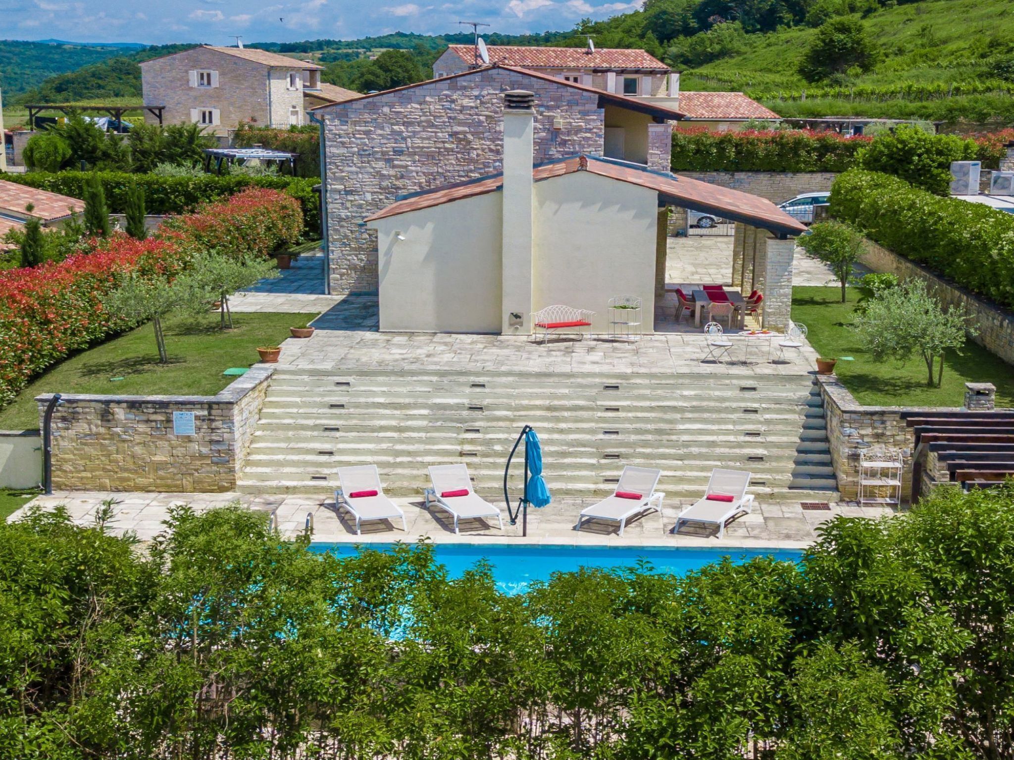 A pool area with lounge chairs and a blue umbrella, surrounded by stone walls and greenery.