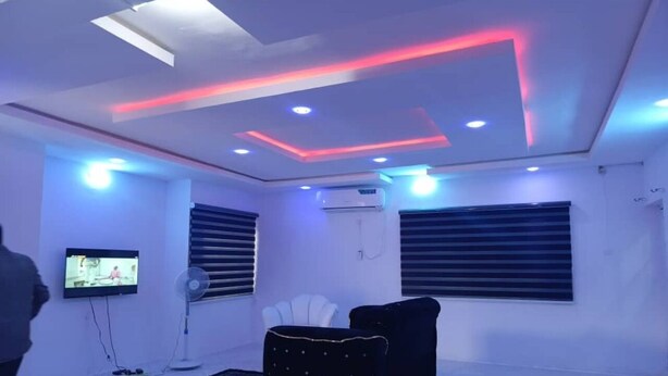 A modern room with a flat-screen TV, a standing fan, and a black sofa. - LUXURY ONE-BEDROOM APARTMENT IN THE HEART OF ABEOKUTA (Abeokuta)