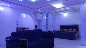 A room with a dark blue sofa, a bed with a patterned bedspread, and a white wall with built-in shelving. - LUXURY ONE-BEDROOM APARTMENT IN THE HEART OF ABEOKUTA (Abeokuta)