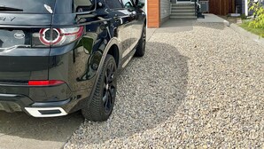 Een modern herenhuis met een grindpad en een geparkeerde SUV.