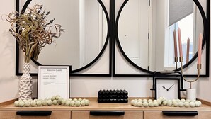 Een houten wastafel met twee grote spiegels, een vaas met gedroogde bloemen, een kaart met Wi-Fi informatie in een lijst en een klok.