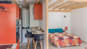 A compact room with a kitchenette, a bed with a colorful blanket, and a small table with chairs.