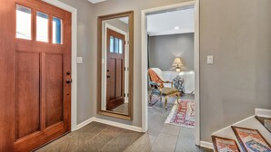 A hallway with a wooden door, a large mirror, and a chair with a lamp.