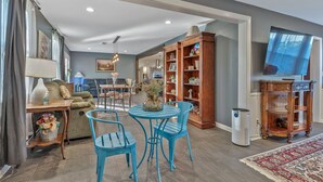 A living room with a blue table and chairs, a wooden bookshelf, and a television.