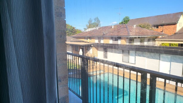 A residential area with a swimming pool, brick houses, and a clear blue sky. - Top View Deluxe Self-Contained Room No 3 with Balcony Overlooking Swimming Pool. (Windsor)