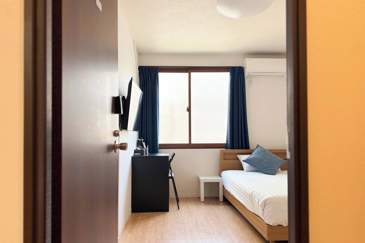 A compact hotel room with a bed, desk, and window.