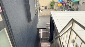 Een smalle trap die leidt naar een ingang van een gebouw, met een metalen leuning aan één kant en een zwarte muur aan de andere kant.