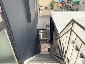 A narrow stairway leading to a building entrance with a metal railing on one side and a black wall on the other. - D-ryokan (Tokyo)