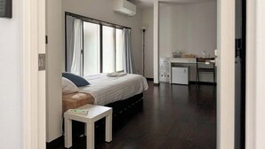 A hotel room with a bed, bedside table, desk, and a small kitchenette.
