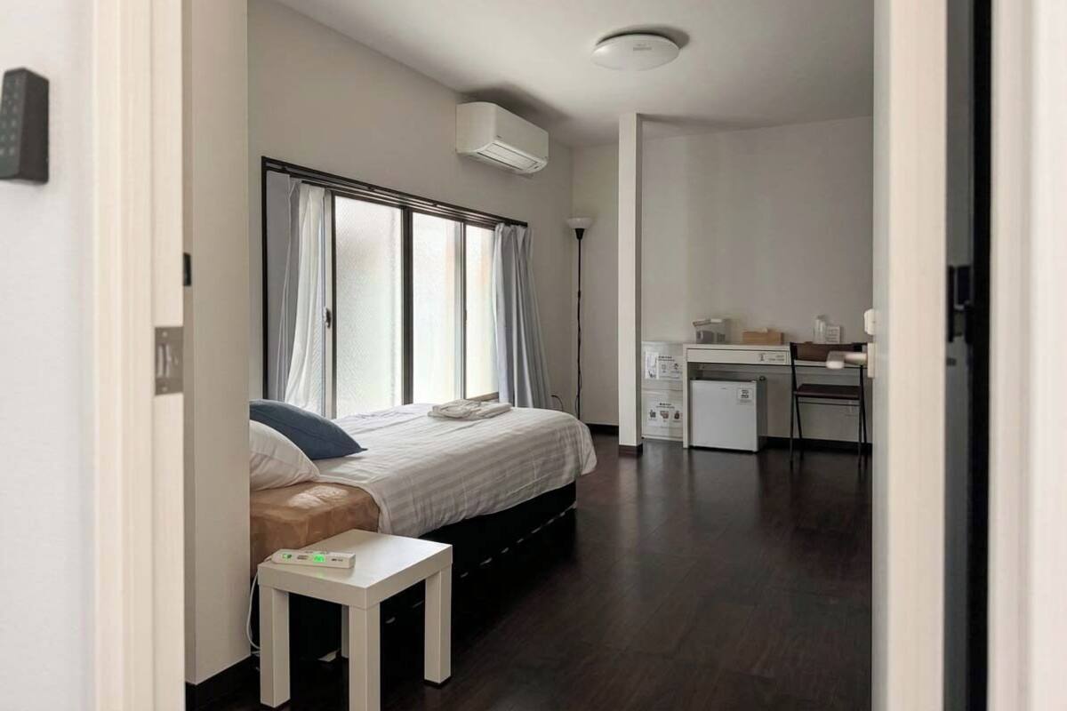 A hotel room with a bed, bedside table, desk, and a small kitchenette.