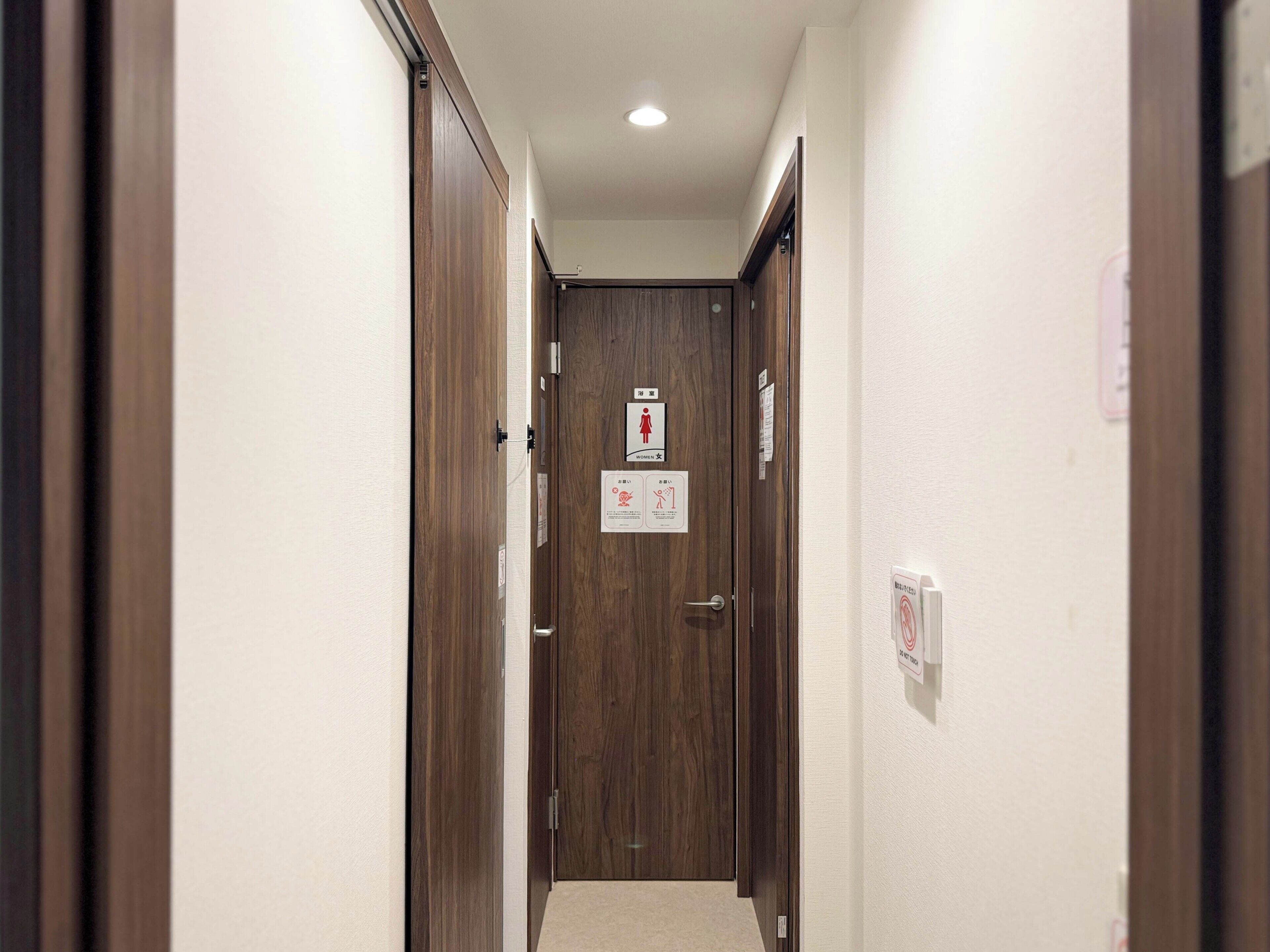 A narrow hallway with wooden doors, a ceiling light, and a sign indicating a women's restroom.