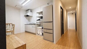 Een moderne keuken met een inbouwmagnetron, een fornuis en een koelkast. Er staat een eettafel met stoelen en er ligt een houten vloer.