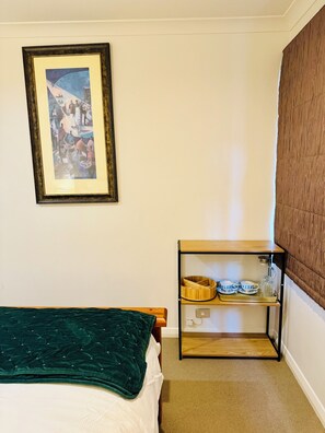 Een slaapkamer met een bed, een ingelijst schilderij, een houten nachtkastje met een dienblad waarop theekopjes en een glas staan, en een bruin hoofdeinde.