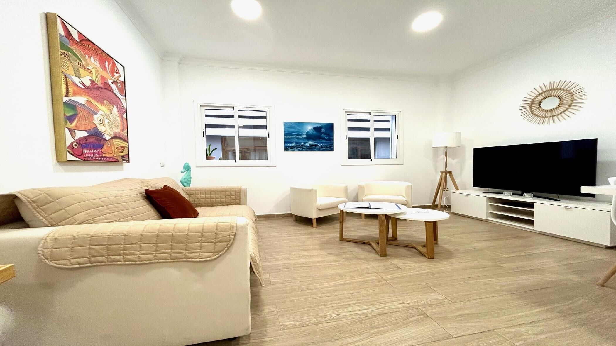 Un soggiorno con un divano color beige, due poltrone, un tavolino da caffè, una TV e opere d'arte alle pareti.