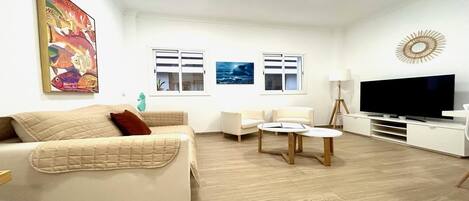A living room with a beige sofa, two armchairs, a coffee table, a TV, and artwork on the walls.