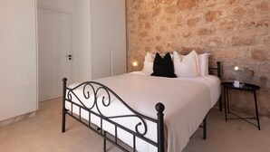 Un dormitorio con pared de piedra, una cama con estructura metálica y una mesita de noche con lámpara.