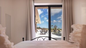 Un dormitorio con cama, una ventana con cortinas y vistas a un espacio exterior con mesa y sillas.