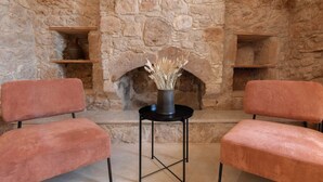 Una chimenea de piedra con dos sillones y un jarrón con plantas secas al frente.
