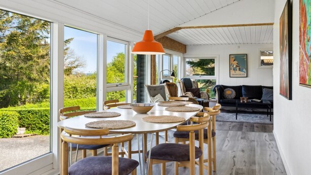 A dining area with a round table, wooden chairs, and a hanging orange pendant light. - "Sölvy" - 300m from the sea by Interhome (Børkop)