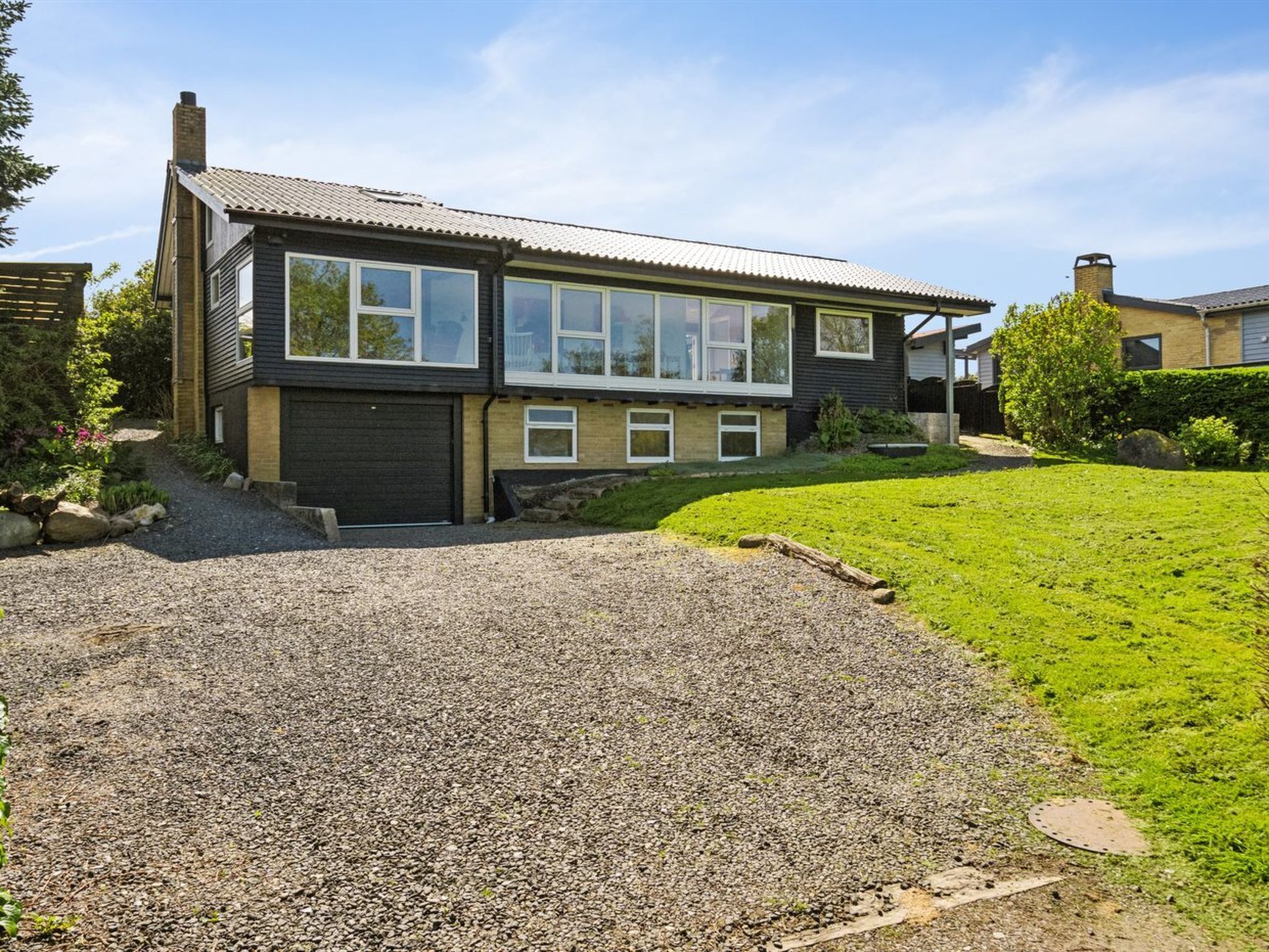 Een modern huis met twee verdiepingen, een grindpad, een garage en een keurig onderhouden gazon.