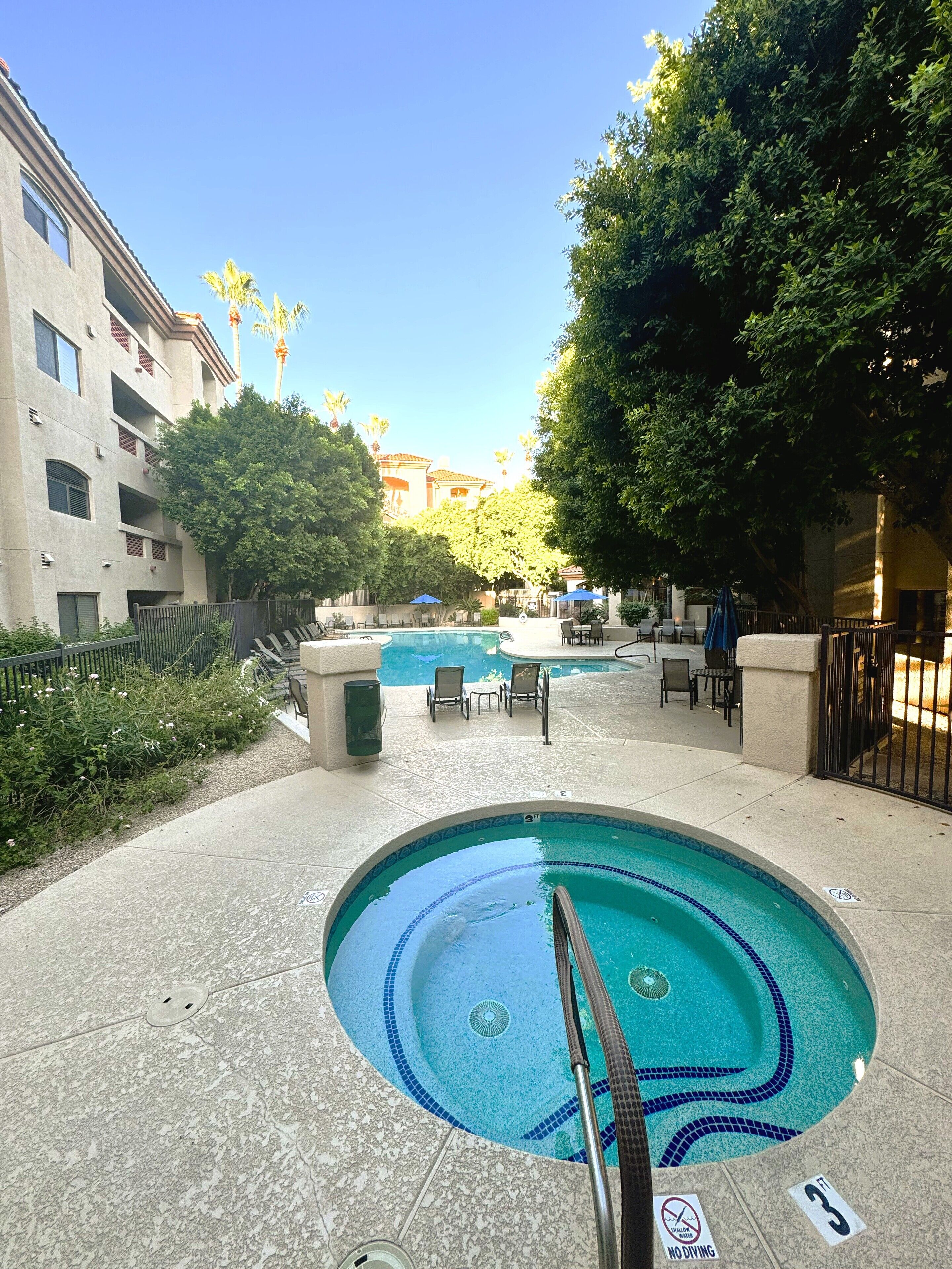 A swimming pool area with a tiled edge, lounge chairs, and a poolside table.