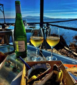 A table with a bottle of wine, two glasses of wine, and a box of oysters. - Appartement 40m2,vue Exceptionnelle. 1 Chambre Indépendante. Climatisation (Sète)