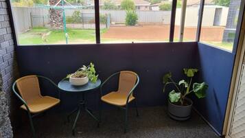 A small balcony with two wicker chairs, a table, and a potted plant.