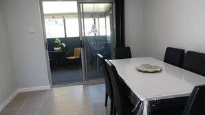 Een eethoek met een witte tafel, zwarte stoelen en een glazen deur naar een balkon met een stoel en een bloempot.