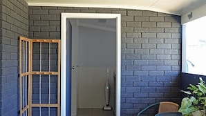 Een kleine kamer met een donkere bakstenen muur, een houten deur, een tafeltje met stoelen, en een plant in een pot.